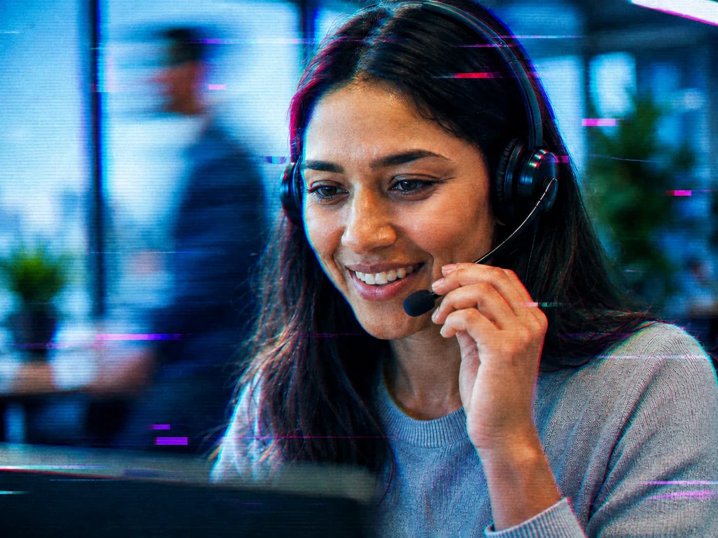 Contact center agent in a headset, smiling in front of their monitor